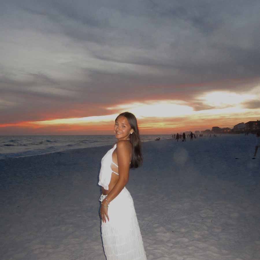 Woman in white smiling on a beach at sunset, near The Dirty Turtle Bar and drinks with friends.