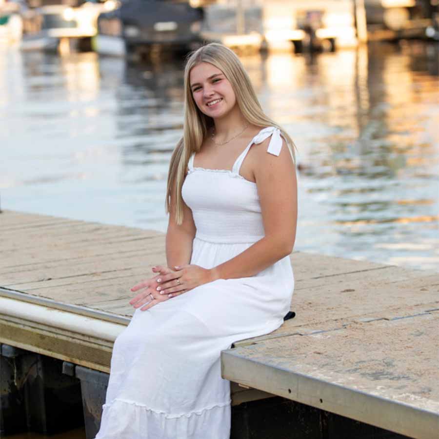 Young woman in a white dress sits on a dock by The Dirty Turtle Bar, smiling with drinks nearby.
