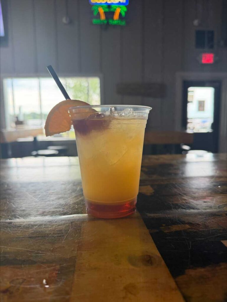 A colorful cocktail from The Dirty Turtle Bar sits with an orange slice and straw on the table.